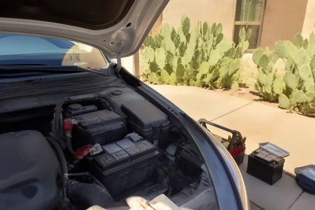 Technician replacing a flooded lead-acid battery in a car engine bay in Phoenix, AZ.