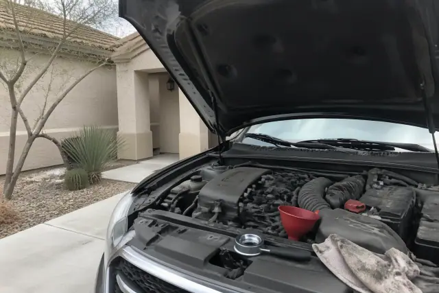 Open hood of a vehicle being serviced with an oil filter wrench and funnel in a Phoenix, AZ driveway.