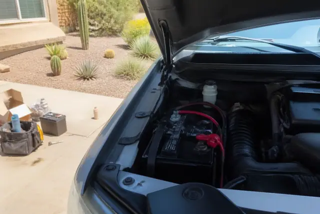 Car battery replacement under the hood of a vehicle on a residential concrete pad in Phoenix, AZ.