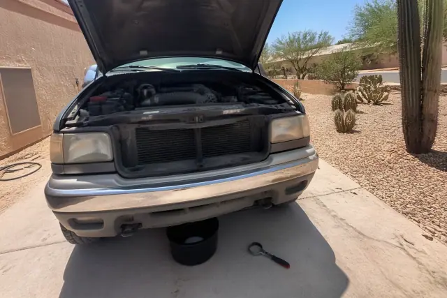 Vehicle with an open hood, oil filter wrench, and drain pan on a concrete pad at a jobsite in Phoenix, AZ.