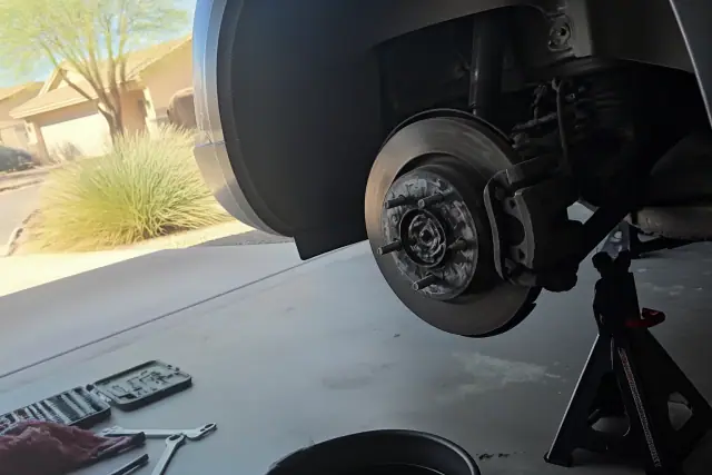 A car on jack stands in a Phoenix, AZ garage undergoing brake repair with the wheel removed and brake parts visible.