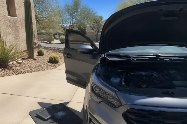 Technician performing a pre-purchase car inspection on a vehicle with an open hood at a residence in Phoenix, AZ.