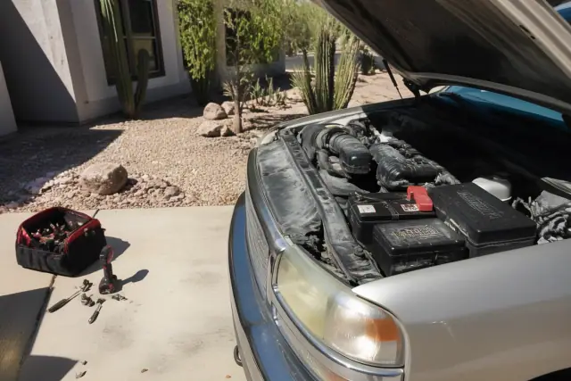 Car hood open with a new battery installed in a residential driveway under bright desert sun in Phoenix, AZ.