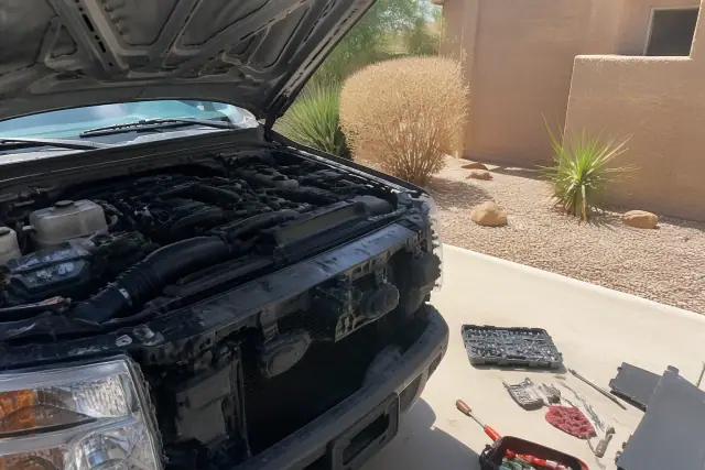 Mobile mechanic working on a car engine on a residential concrete driveway in Phoenix, AZ.