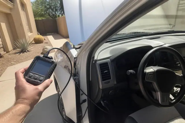 OBD-II scanner plugged into a car with its hood raised on a concrete driveway in Phoenix, AZ.