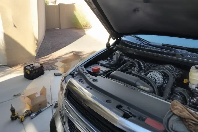 OEM alternator installed in a vehicle engine bay during a repair in a residential driveway in Phoenix, AZ.