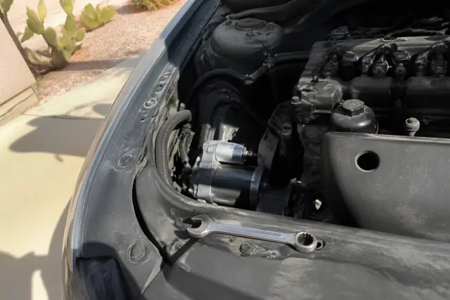 OEM starter motor installed in a vehicle engine bay with a wrench nearby on a sunny day in Phoenix, AZ.