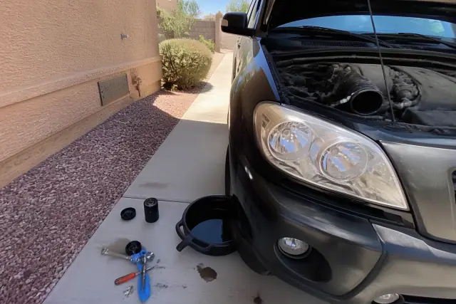 Vehicle oil change in progress with tools and a drain pan on a residential concrete driveway in Phoenix, AZ.