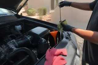 Fresh oil filter housing and clean dipstick under the open hood of a car in a Phoenix, AZ driveway.