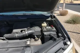Clean engine bay with a new battery and belts under an open car hood in a Phoenix, AZ driveway.