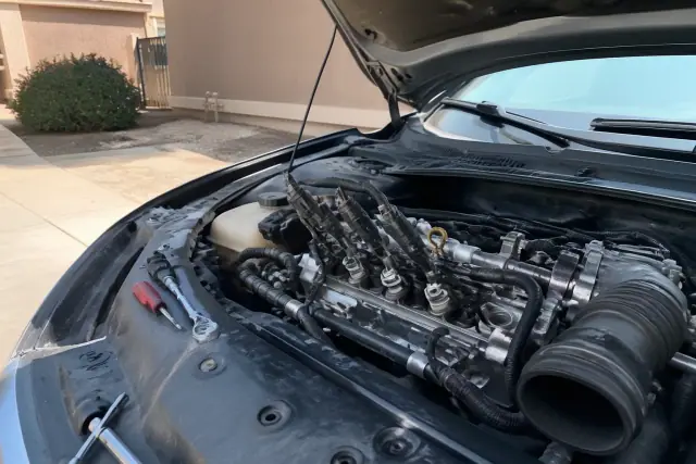 A technician performs a pre-purchase ignition check on an open vehicle engine in a Phoenix, AZ residential driveway.