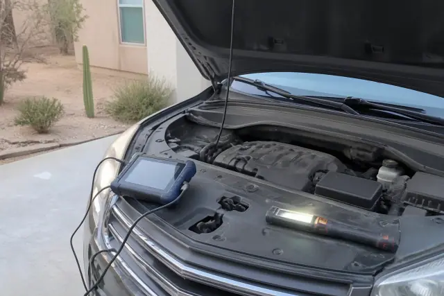 A car undergoing a pre-purchase inspection with a diagnostic scanner in a residential driveway in Phoenix, AZ.