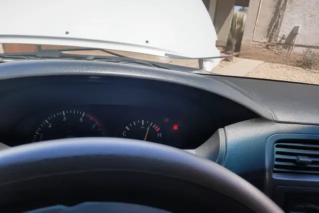 Dashboard temperature gauge and warning light visible inside a vehicle parked at a home in Phoenix, AZ.