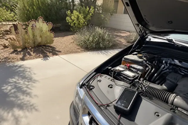 Car hood raised for an engine diagnostic scan on a concrete driveway in Phoenix, AZ with desert landscaping.