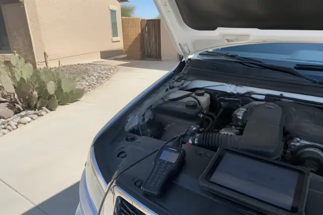 A car with its hood raised during a check engine light diagnostic in a residential driveway in Phoenix, AZ.