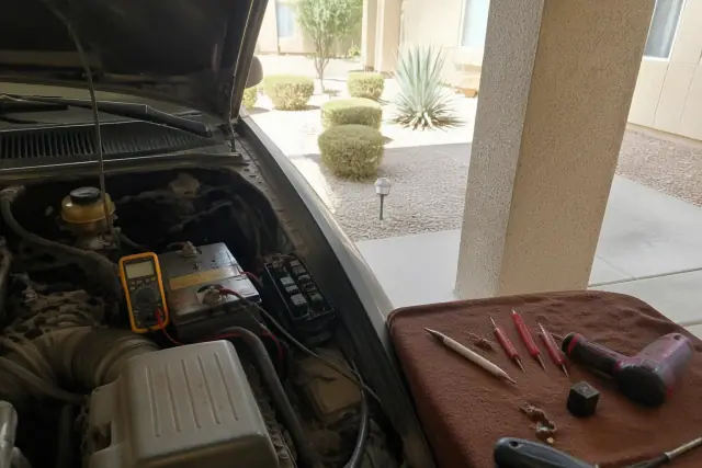 Multimeter testing a starter relay and engine components in a residential carport in Phoenix, AZ.
