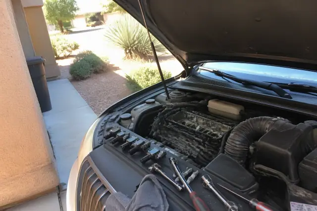 A technician replaces spark plugs and ignition coils on a car engine in a residential driveway in Phoenix, AZ.