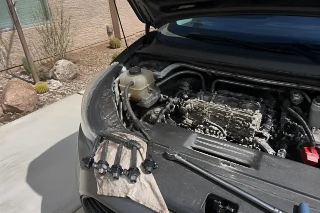 Mobile mechanic performing a spark plug and ignition coil replacement on a car in a residential driveway in Mesa, AZ.