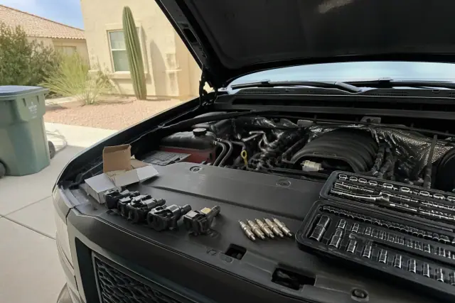 A mechanic performing a spark plug and ignition coil replacement on a vehicle in a driveway in Goodyear, AZ.