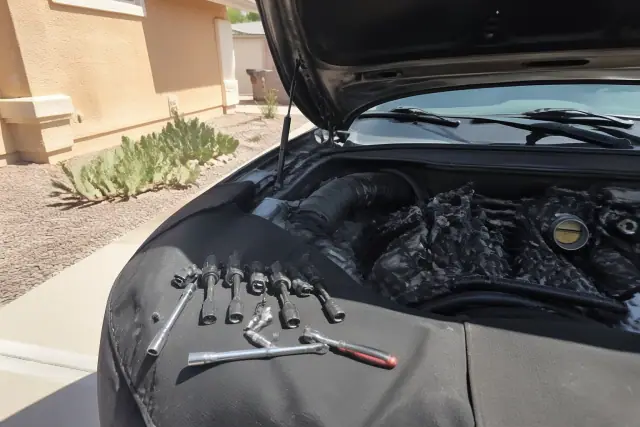 Mechanic replacing spark plugs and ignition coils on a vehicle in a Glendale, AZ residential driveway.