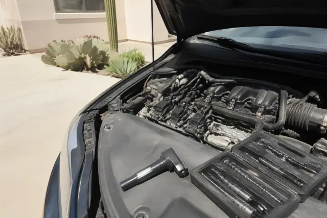 Technician replacing spark plugs and an ignition coil on a car in a Scottsdale, AZ residential driveway.