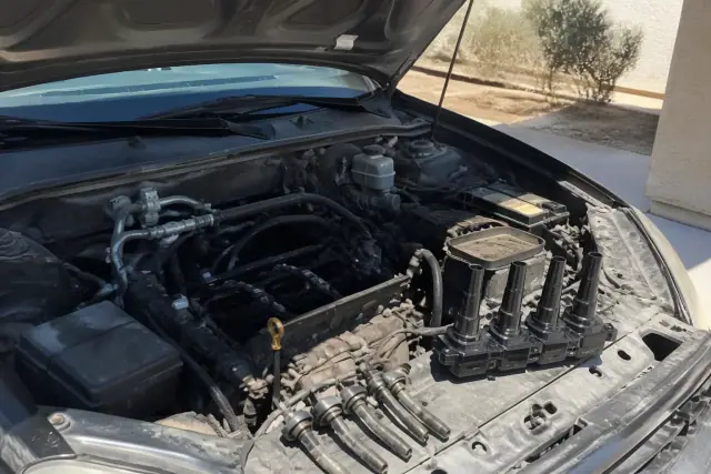 A car engine bay with a new ignition coil and removed spark plug wires at a home in Chandler, AZ.
