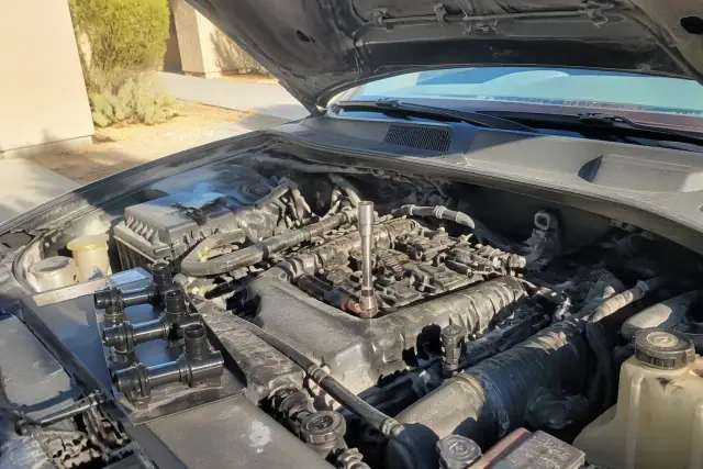 A vehicle engine bay with an ignition coil and spark plug socket during a repair in Tempe, AZ.