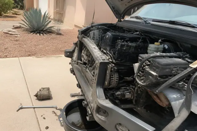 New starter motor installed on a vehicle engine in a residential driveway in Mesa, AZ.