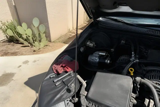 New starter motor installed on a vehicle engine with tools on a concrete pad in Chandler, AZ.