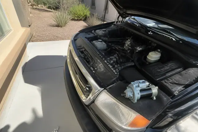 Vehicle with an open hood undergoing a starter replacement on a concrete driveway in Glendale, AZ.