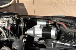 Newly installed starter motor with terminal connections and a socket wrench in a Phoenix, AZ driveway.