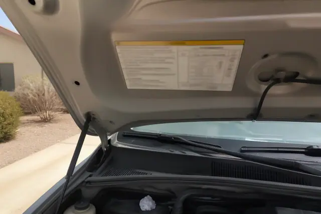 Close-up of a vehicle refrigerant label and charge capacity table under an open car hood in Phoenix, AZ.