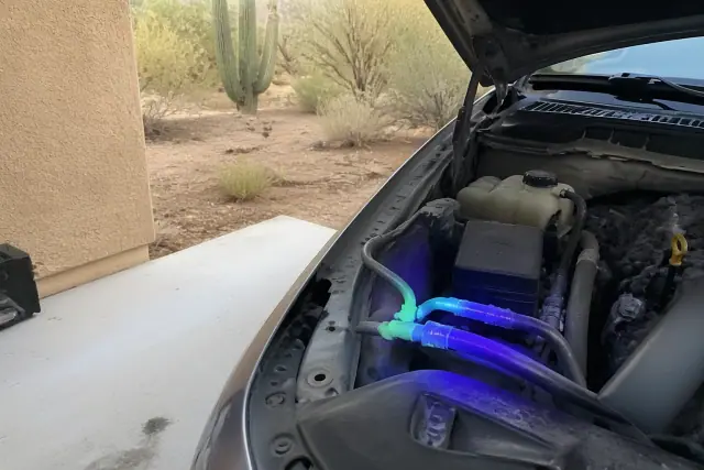 Neon-tinted UV dye residue at car AC hose fittings during a leak check on a residential driveway in Phoenix, AZ.