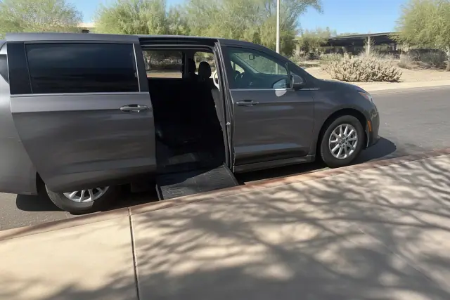 Ambulatory transport van with sliding doors open for boarding on a sunlit curb in Phoenix, AZ.
