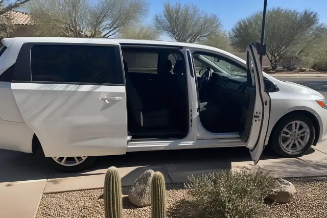 Ambulatory transport van with open side doors parked on a concrete curb in Phoenix, AZ with cacti and desert landscaping.