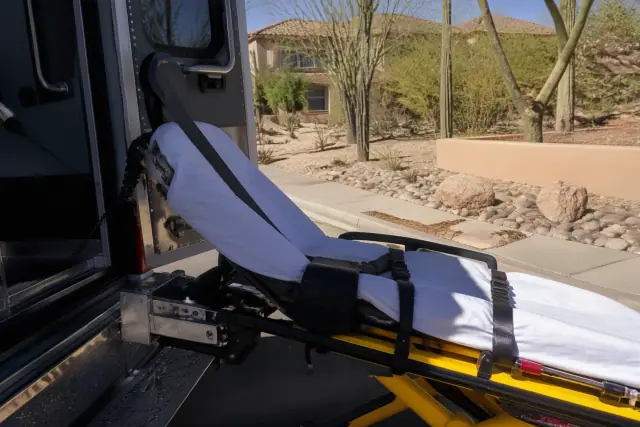 Bariatric stretcher with safety straps secured at the rear of a vehicle on a xeriscaped street in Phoenix, AZ.