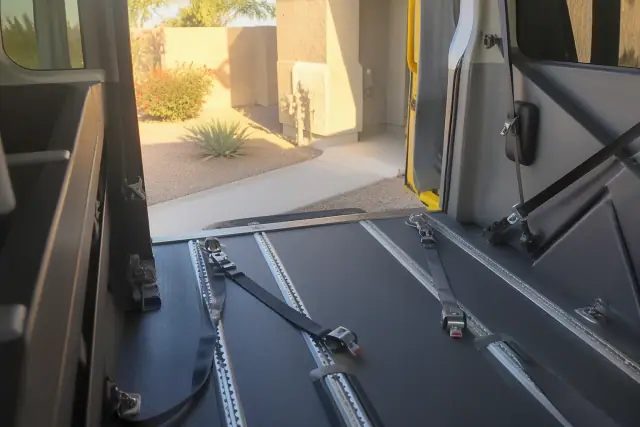 Interior of a bariatric transport vehicle with wheelchair tie-downs, parked by a xeriscaped front yard in Phoenix, AZ.