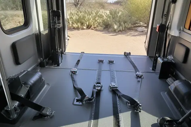 Wheelchair securement station with tie-down straps inside a medical transport van in Phoenix, AZ with cacti outside.