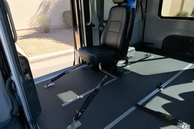 Heavy-duty tie-down straps secured on a medical transport vehicle floor in Phoenix, AZ, seen through a window.