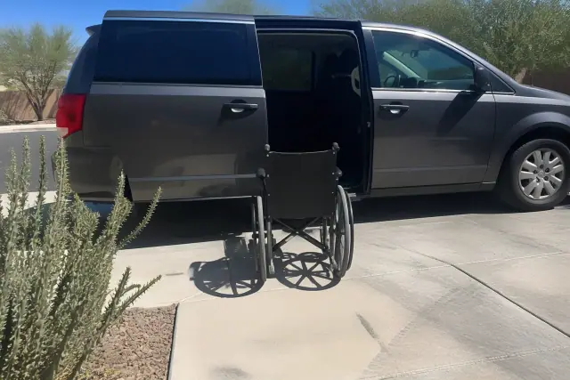 Medical transport van with doors open for passenger boarding at a curbside in Phoenix, AZ, near desert landscaping.