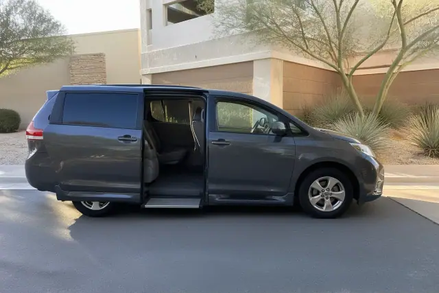 Medical transport van parked at a curb in Phoenix, AZ, with open sliding doors near a building with desert landscaping.