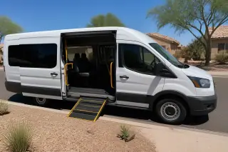 Transport van with open side doors parked at a curb in Phoenix, AZ, in front of a xeriscaped yard.