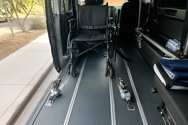 Empty wheelchair secured with tie-down straps inside a medical transport van in Gilbert, AZ.