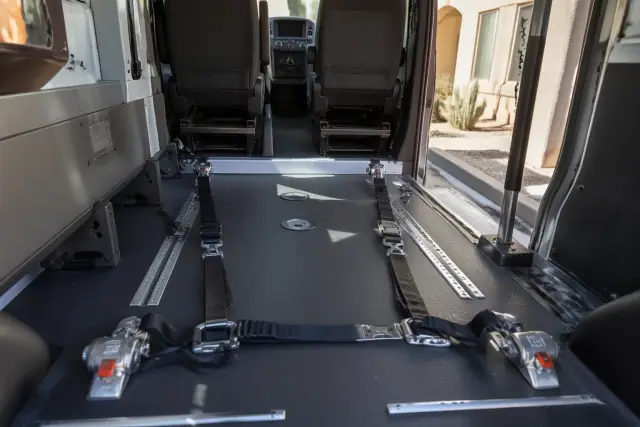 A technician inspecting wheelchair securement anchors in a medical transport vehicle in Phoenix, AZ.