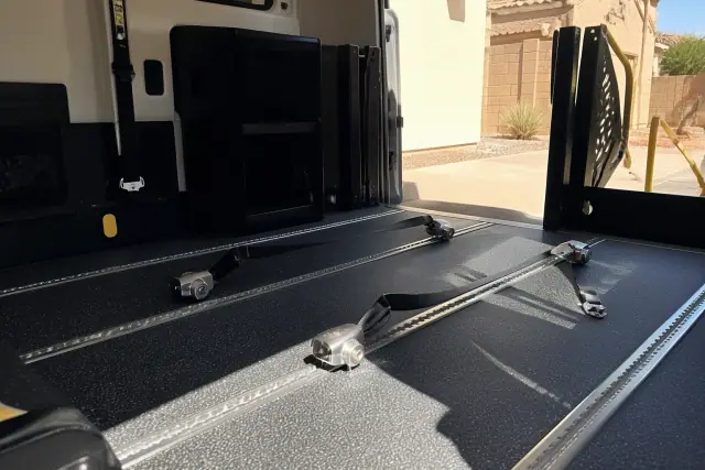 Wheelchair securement station with four-point tie-down straps inside a medical transport vehicle in Chandler, AZ.