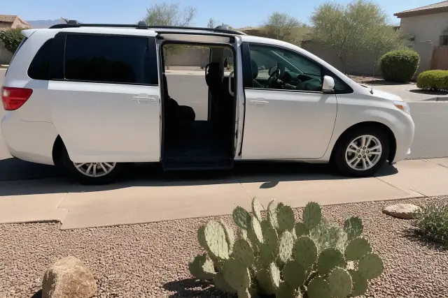 Medical transportation vehicle with open side doors parked by a curbside in Phoenix, AZ with desert landscaping.