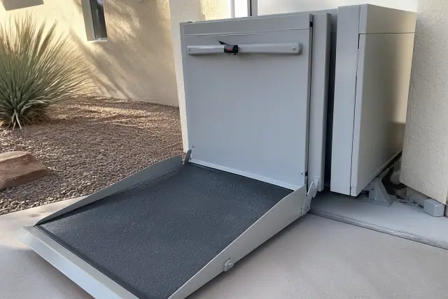 Automated hydraulic wheelchair lift lowered to the ground against a stucco wall in Phoenix, AZ.