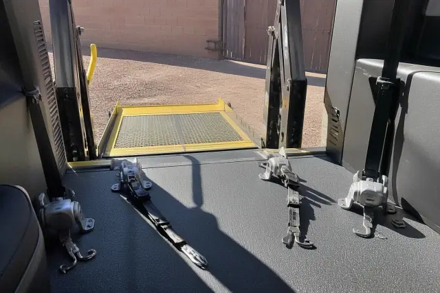 Hydraulic ramp and four-point wheelchair securement straps inside a van on a sunny jobsite in Phoenix, AZ.