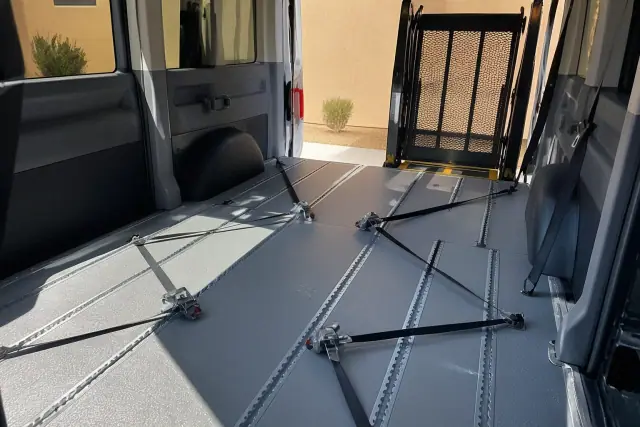 Interior of an ambulatory transport vehicle in Phoenix, AZ, showing floor tracks and four-point tie-down straps.