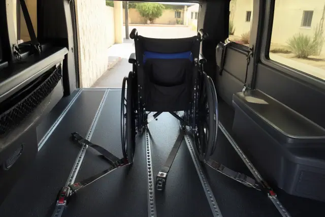 Wheelchair secured in a transport van with four-point tie-downs and desert view through the door in Phoenix, AZ.